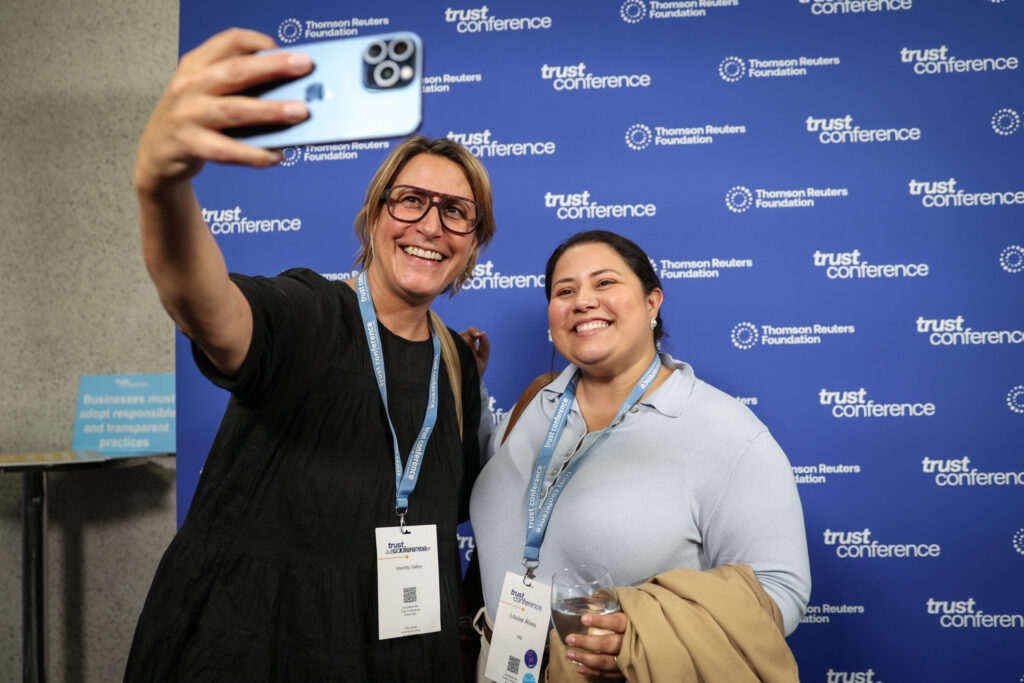 two women take selfie against branded backdrop